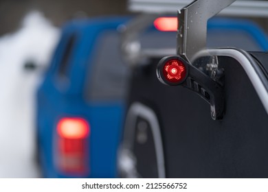 Stop, Brake And Dimensions Lights On Mini Camper Towed By A Blue Muscle Car In The Woods. Family Journey Time Together Away In The Forest Wild Life. Pick Up Truck With RV Travel Trailer Driving Though