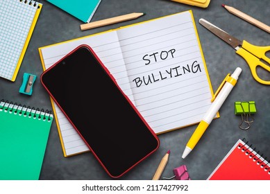 Stop Bullying. Top View Of Notebook With The Text Stop Bullying, School Supplies And Smartphone Over Gray Background