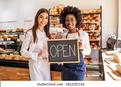 Stop by for homemade delicious bread! Loving young women embracing holding a sign together on the opening day of their small business - couple owners of the bakery smiling to the camera - Powered by Shutterstock