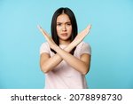 Stop. Concerned asian woman showing cross sign, saying no, raise awareness, standing over blue background