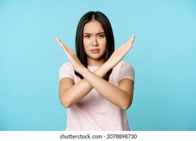 Stop. Concerned asian woman showing cross sign, saying no, raise awareness, standing over blue background