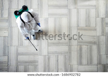 Stop COVID-19. Top view of an unrecognizable person in white chemical protection suit doing disinfection and spraying of public areas to stop highly contagious corona virus. Copy space provided.