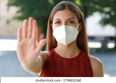 STOP COVID-19 Young Woman Wearing KN95 FFP2 Mask on her Face Showing Gesture STOP Looking at Camera Outdoors. Girl with face mask showing open hand palm at the camera against Coronavirus disease 2019.