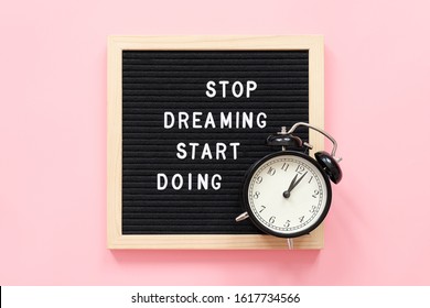 Stop Dreaming Start Doing. Motivational quote on frame letter board and black alarm clock on pink background. Top view Flat lay Concept inspirational quote of the day.
