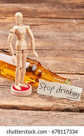 Stop drinking and become thinking. Human wooden dummy, alcohol beverage in glass bottle, message, wooden background.