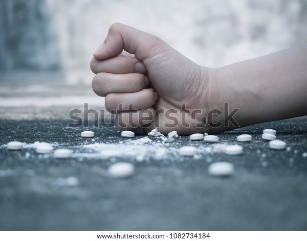薬物中毒のコンセプトをやめなさい グランジーなコンクリートの床に白い丸薬をこぶしで押しつぶす若い人間の手 薬物乱用に対する国際的な抗議の日 接写 の写真素材 今すぐ編集