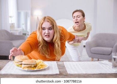 Stop. Excited stout woman reaching for a sandwich and her friend holding her