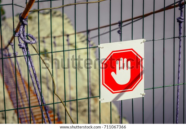 Stop hand sign on metal fence. Blurred rope\
bridge, rock, sky and sea on\
background.