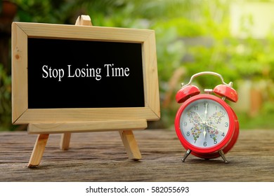 STOP LOSING TIME! inscription written on chalkboard and red alarm clock on  old wooden desk . Time concept. - Shutterstock ID 582055693
