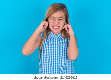 Stop Making This Annoying Sound! Unhappy Stressed Out Little Kid Girl With Glasses Wearing Plaid Shirt Over Blue Background Making Worry Face, Plugging Ears With Fingers, Irritated With Loud Noise.