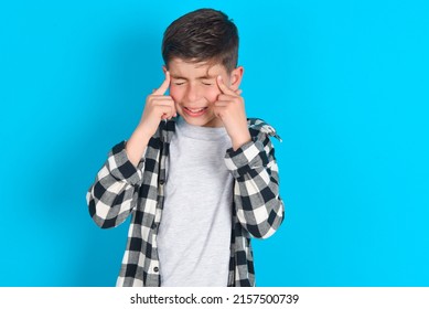 Stop Making This Annoying Sound! Unhappy Stressed Out Caucasian Kid Boy Wearing Plaid Shirt Over Blue Background Making Worry Face, Plugging Ears With Fingers, Irritated With Loud Noise.