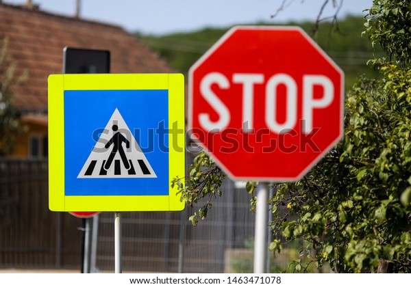 Stop and pedestrian crossing sign one next to\
another on a street
