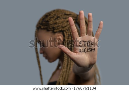 Stop racism. Young African American woman standing sideways, head down, showing palm with stop racism lettering