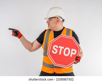 Stop Road Sign. Builder Warns Of Danger. Worker Indicates Direction. Road Hazard Warning. Concept Is Prevention Of Accidents. Stop Warning. Mature Man In Uniform Of Construction Worker.