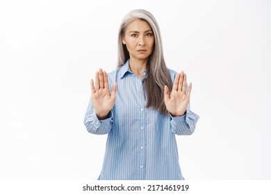 Stop. Serious Asian Woman Showing Prohibit, Forbid Gesture, Extending Palms Forward And Saying No, Step Back, Standing Over White Background