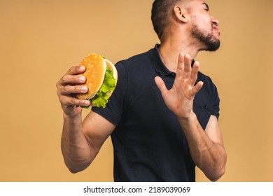 Stop sign, bad smell. Young african american black man eating hamburger isolated over beige background. Diet concept. - Powered by Shutterstock