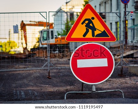 Stop sign and road work sign inform that road is closed.  Road construction work and orange excavator on background.
