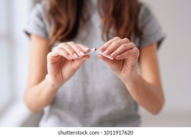 Stop smoking cigarettes concept. Portrait of beautiful smiling girl holding broken cigarette in hands. Happy female quitting smoking cigarettes. Quit bad habit, health care concept. No smoking.