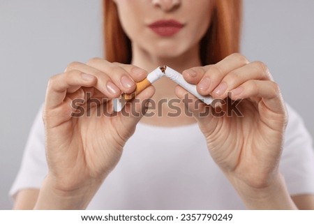 Stop smoking concept. Woman breaking cigarette on light gray background, closeup