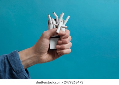 Stop smoking. Man holding pack with broken cigarettes on light blue background, closeup