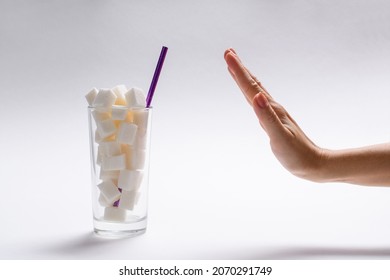 Stop sugar! A full glass of sugar and a woman's hand with a refusal gesture. The concept of avoiding the use of sugary drinks and cocktails. Selective focus on the glass.