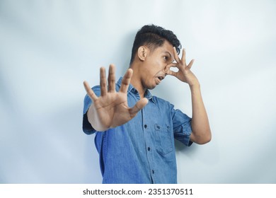 Stop unpleasant smell. Portrait of young man in denim casual shirt displeased by stink, grimacing in disgust and pinching his nose, making no gesture. indoor studio shot isolated on yellow background