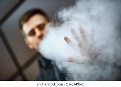 Stop Vape. Hand Of A Young White Guy In Black Jacket Vaping An Electronic Cigarette Opposite The Futuristic Urban Background In The Spring. Lifestyle.