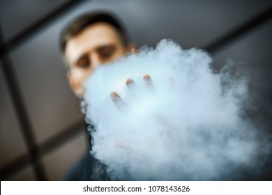 Stop Vape. Hand Of A Young White Guy In Black Jacket Vaping An Electronic Cigarette Opposite The Futuristic Urban Background In The Spring. Lifestyle.