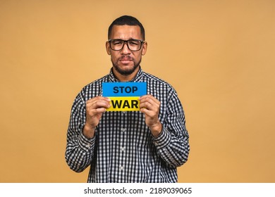 Stop war! Save Ukraine! Portrait of sad negative african american black guy holding ukrainian flag, isolated over beige background. - Powered by Shutterstock