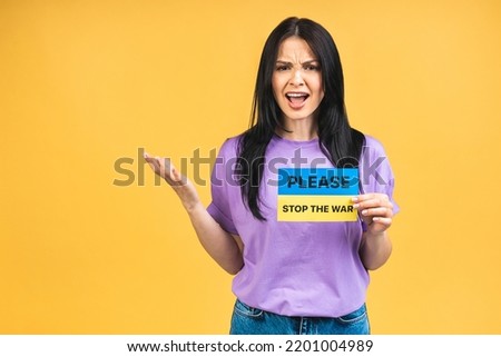 Stop war in Ukraine! Portrait of sad agressive angry woman holding in hands Ukrainian flag isolated over yellow pastel color background.