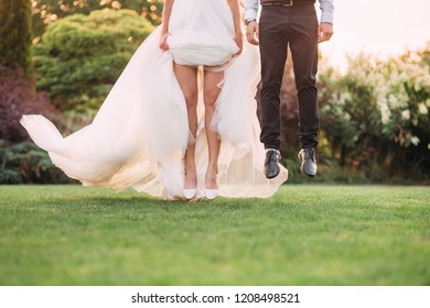 stopped moment, a leap, jump in the air as if the bride and groom are flying above the green grass in the garden, no faces on the picture, the girl’s bare legs, art processing photo