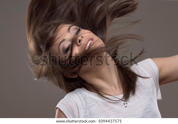 Stopped
motion of beautiful young straight hair brunette tossing hair and
looking at camera over gray studio
background.