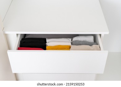 Storage of apparel in the apartment. High angle view of folded colorful clothes organized in open dresser drawer at wardrobe. Concept of tidiness in closet and commode