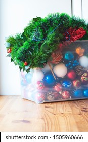 Storage Of Christmas Decorations. Christmas Balls, Decorations, Tinsel And Garlands In A Large Plastic Box On A Wooden Table, Light Background.