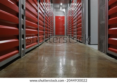 Storage corridor warehouse. Self storage facility, red and gray metal doors with locks. Moving, organizing, storage concept.