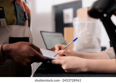 Storage room supervisor signing delivery documents, african american employee working at customers orders preparing packages in storehouse. Diverse team standing at counter in warehouse. Close up - Powered by Shutterstock