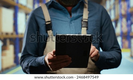 Storage room worker counting boxes of merchandise, checking depot stock on racks inside industrial warehouse. Customs compliance specialist doing quality control for retail industry.