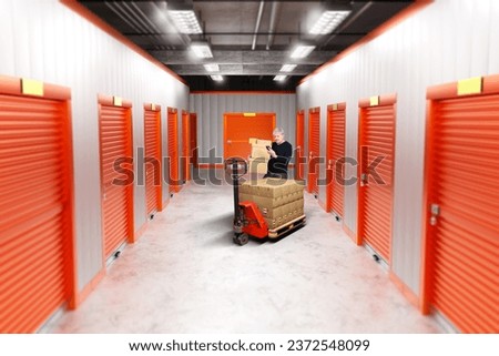 Storage units rent. Man in warehouse hallway. Guy carries boxes into storage units. Doors to warehouse units are closed. Man client of storage company. Businessman with boxes near pallet jack