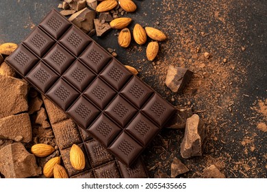 Store Cooking chocolate bars with almonds handmade sweets. Composition of bars and pieces of dark almond chocolate on a black background, top view. Pastry craft on the table