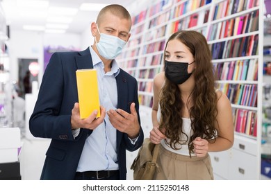 Store Employee In Face Mask Offering Young Female Customer Box With New Phone In Consumer Electronics Store