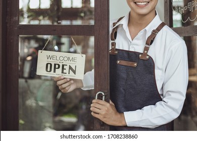 Store Owner Turning Open Sign Broad Through The Door Glass And Ready To Service.