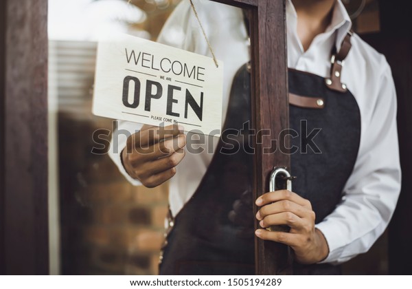 Store owner turning open sign broad through the\
door glass and ready to\
service.