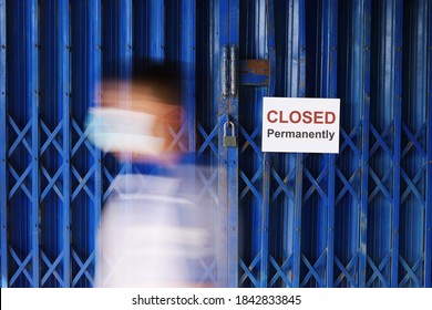 Store Shop Or Business Office Is Permanently Closed, Bankrupt Business As A Result Of COVID-19 Pandemic’s Economic Toll. Blurred Motion Of Person Wearing Mask Passing By Closed Sign On Locked Door.