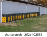 Stored recycle dustbins arranged in a row with yellow lids open next to a shed at a showground until the next showground event in the outback countryside in New South Wales in Australia.