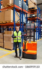 Storehouse Employee In Uniform Working On Forklift In Modern Automatic Warehouse. Worker Showing Thumbs Up. Boxes On The Shelves Of The Warehouse. Warehousing, Machinery Concept. Logistics In Stock.