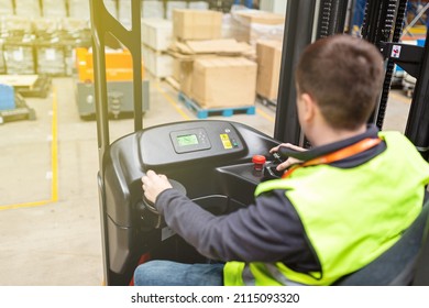 Storehouse Employee In Uniform Working On Forklift In Modern Automatic Warehouse. Boxes Are On The Shelves Of The Warehouse. Warehousing, Machinery Concept. Logistics In Stock.