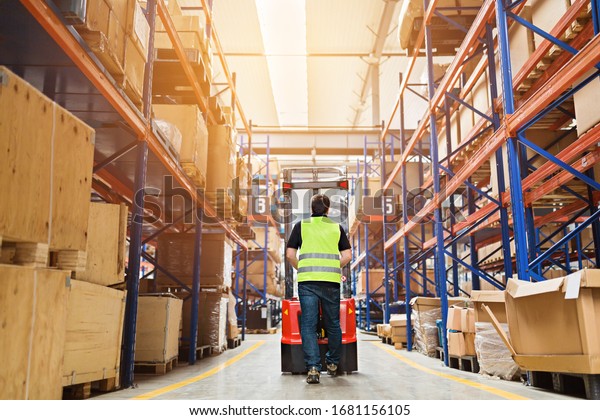 Storehouse\
employee in uniform working on forklift in modern automatic\
warehouse.Boxes are on the shelves of the warehouse. Warehousing,\
machinery concept. Logistics in\
stock.