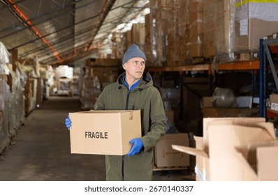 Storekeeper man stacking pasteboard box in storehouse during working day.