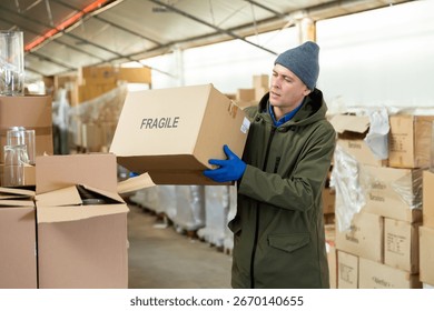 Storekeeper man stacking pasteboard box in storehouse during working day.