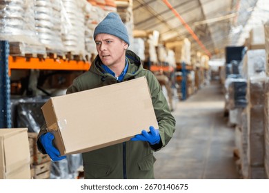 Storekeeper man stacking pasteboard box in storehouse during working day.